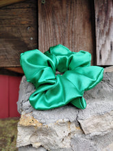 Load image into Gallery viewer, A green silky scrunchie displayed in front of a rustic background.