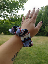 Load image into Gallery viewer, A person's forearm showcasing a blue and white striped scrunchie hair accessory.