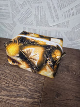 Load image into Gallery viewer, side view of cosmetic bag with gold open book print lack back ground
